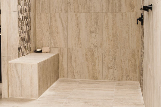 A sand-colored tiled standing shower with a full-sized Schluter waterproof shower bench holding a bar of soap and loofah.