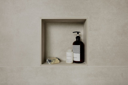 A small gray shower niche holding shampoo, Olaplex hair treatment and a bar of soap.